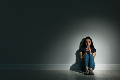 Photo of Lonely woman with smart phone sitting on floor in dark room. Space for text