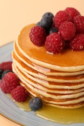 Stack of tasty pancakes with raspberries, blueberries and honey on pale orange background, closeup