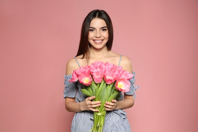 Photo of Portrait of beautiful smiling girl with spring tulips on pink background. International Women's Day