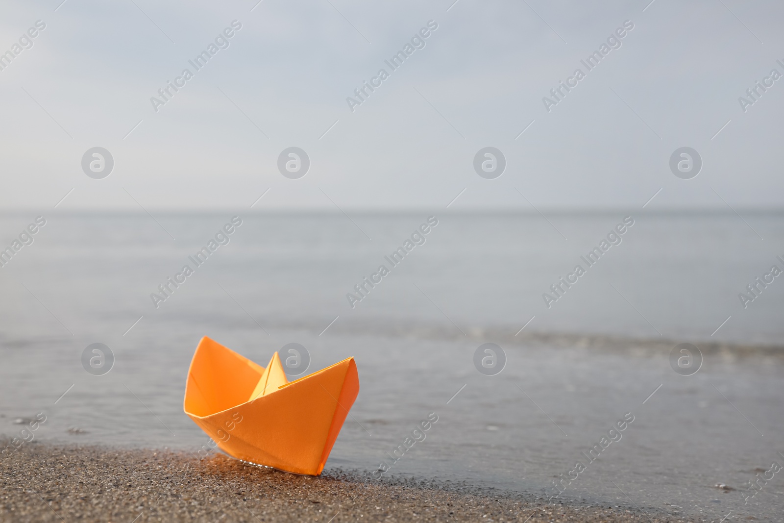 Photo of Orange paper boat on sandy beach near sea, space for text