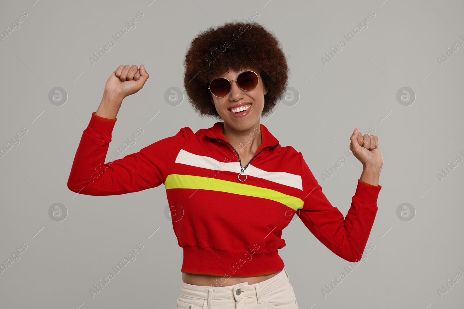 Photo of Happy young woman in stylish sunglasses dancing on grey background