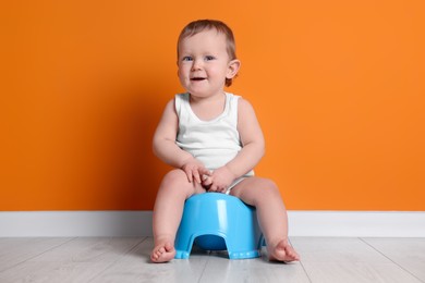 Photo of Little child sitting on baby potty near orange wall