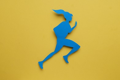Photo of Sportswoman paper figure on yellow background, top view. Woman`s health