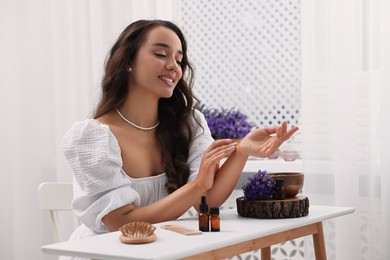 Photo of Beautiful young woman applying essential oil onto wrist at table indoors