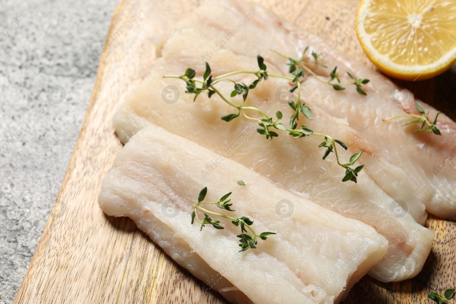 Photo of Raw cod fish, microgreens and lemon on grey textured table, closeup