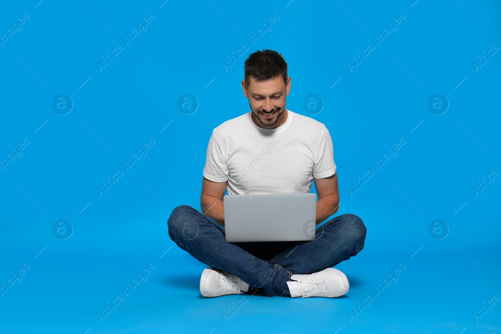 Photo of Happy man sitting with laptop on light blue background