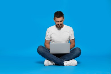 Photo of Happy man sitting with laptop on light blue background