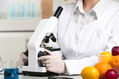 Scientist inspecting slice of cucumber with microscope in laboratory, closeup. Poison detection