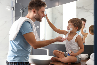 Photo of Dad and son with shaving foam on their faces having fun in bathroom