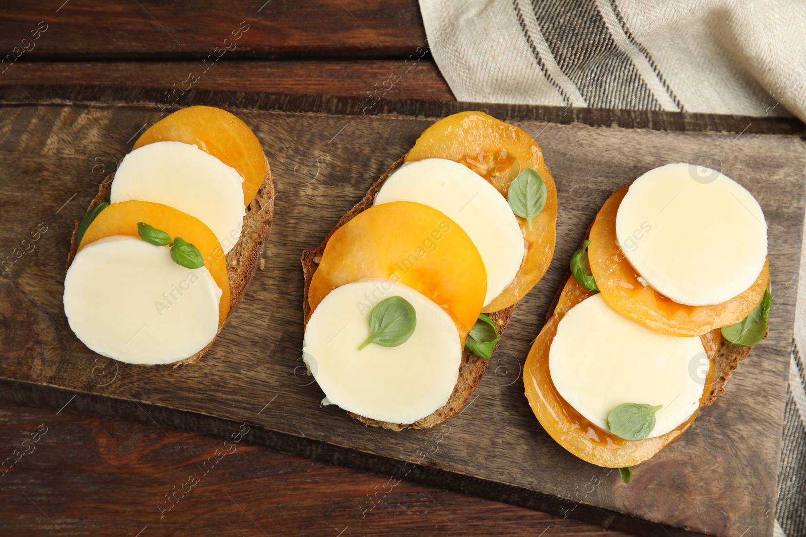 Photo of Delicious sandwiches with mozzarella, yellow tomatoes and basil on wooden table, flat lay