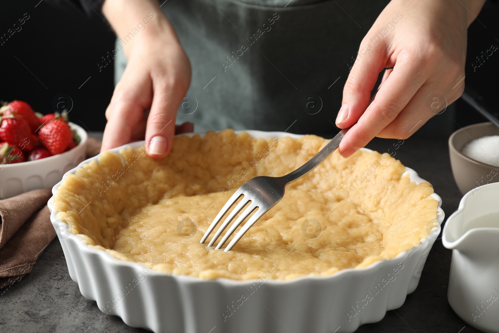 Photo of Shortcrust pastry. Woman making holes in raw dough with fork at grey table, closeup