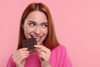 Young woman eating tasty chocolate on pink background