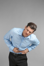 Young man suffering from abdominal pain on grey background