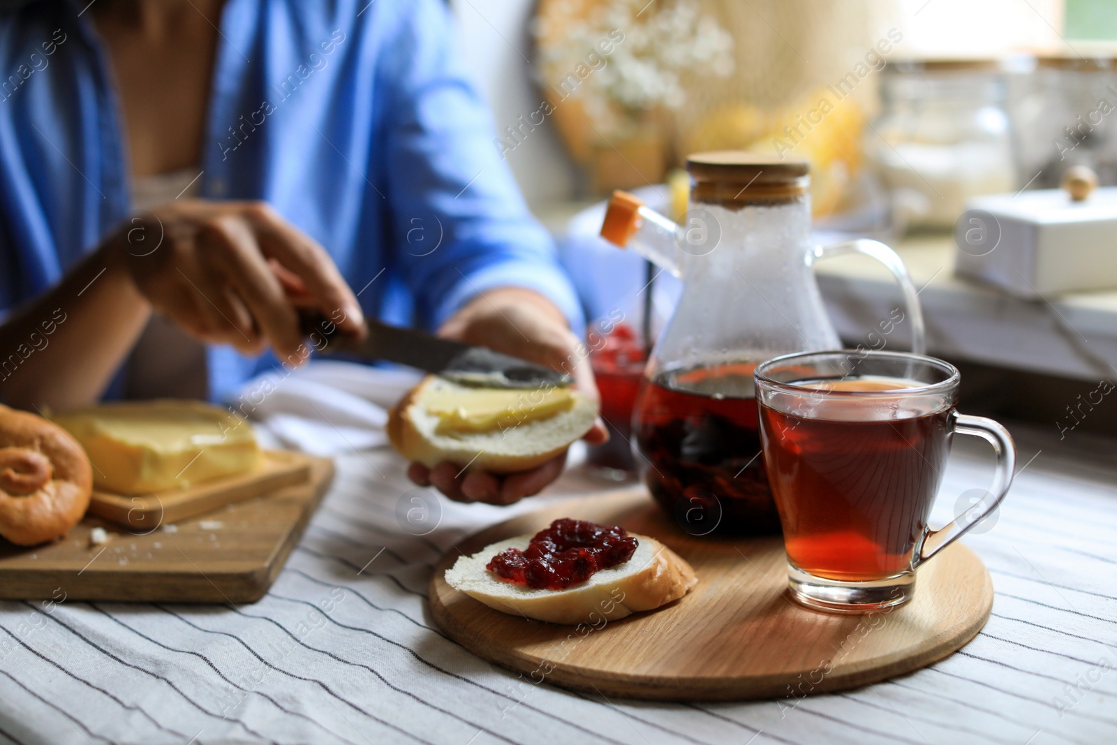 Photo of Woman spreading butter onto bread at table indoors, focus on aromatic tea