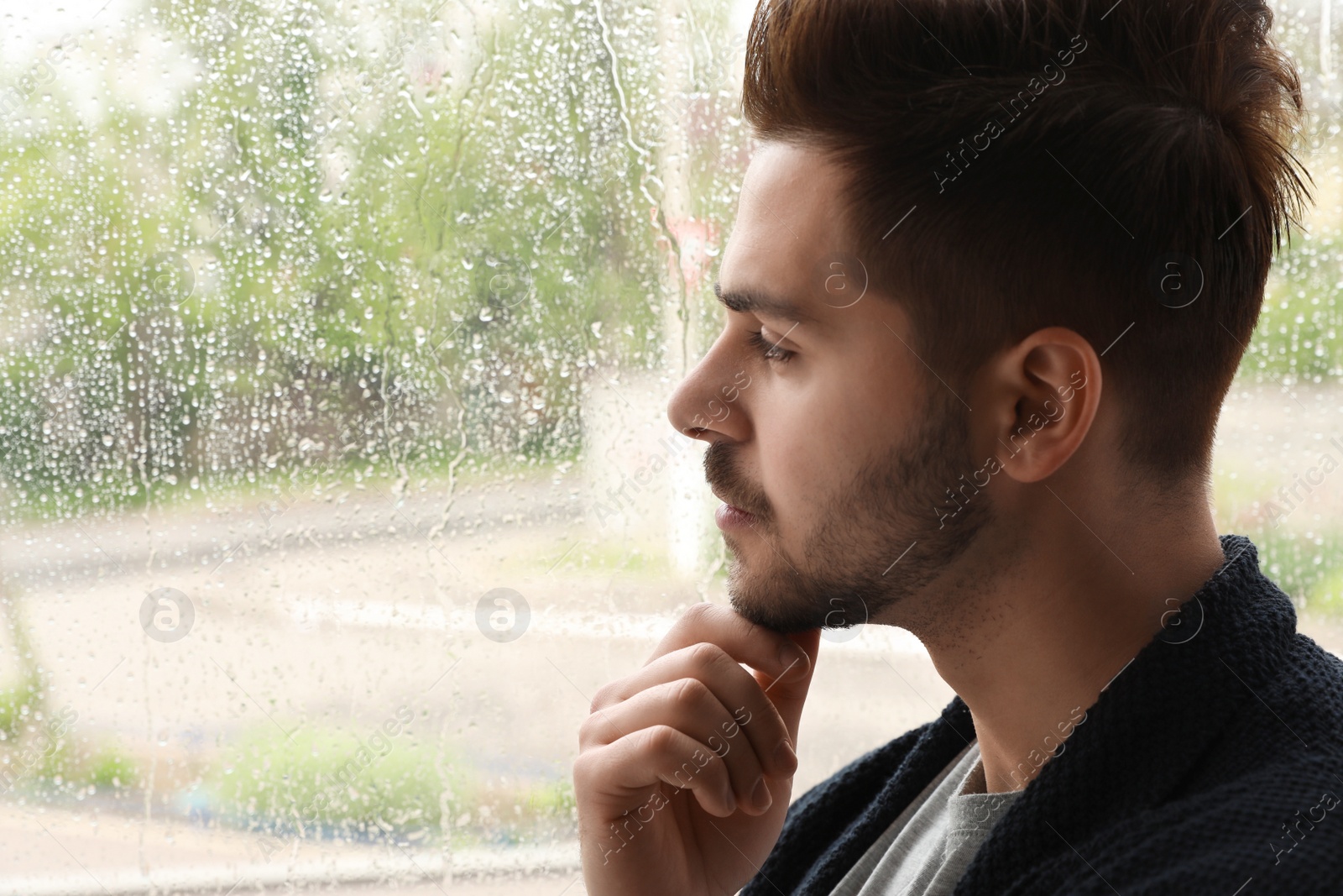 Photo of Thoughtful handsome man near window indoors on rainy day