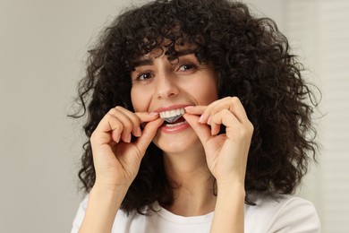 Young woman applying whitening strip on her teeth against light grey background