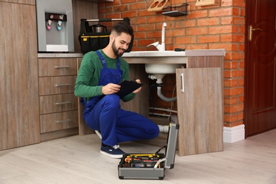 Male plumber with clipboard near kitchen sink. Repair service