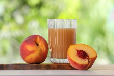 Glass of tasty peach juice and fresh fruits on white table outdoors, closeup