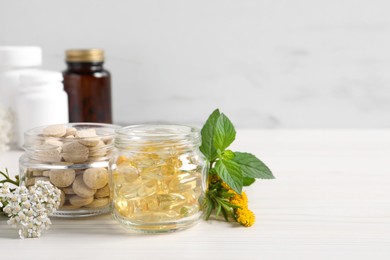 Jars with different pills, flowers and herbs on white wooden table, space for text. Dietary supplements