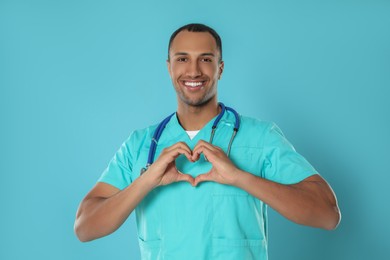 Photo of Doctor or medical assistant (male nurse) in uniform making heart with hands turquoise background