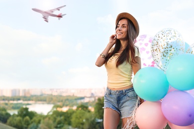 Image of Beautiful young woman with color balloons under sky with flying airplane