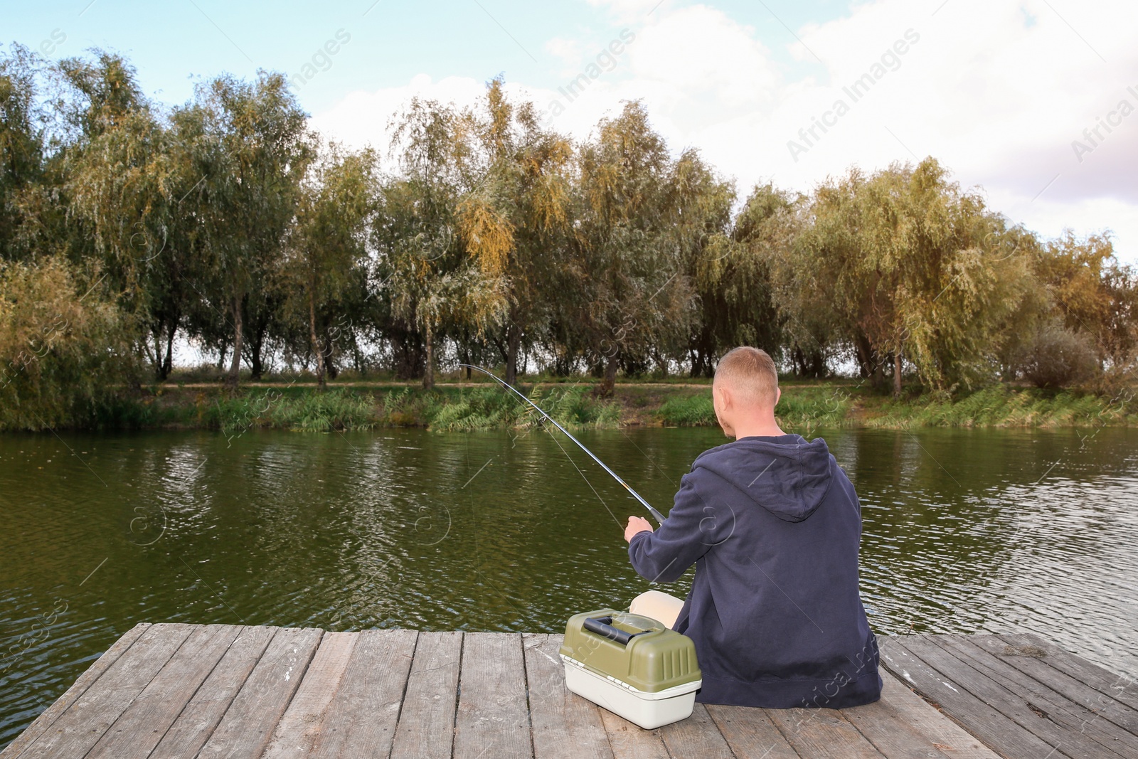 Photo of Man fishing on wooden pier at riverside. Recreational activity