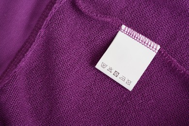Photo of White clothing label with care information on purple garment, top view. Space for text