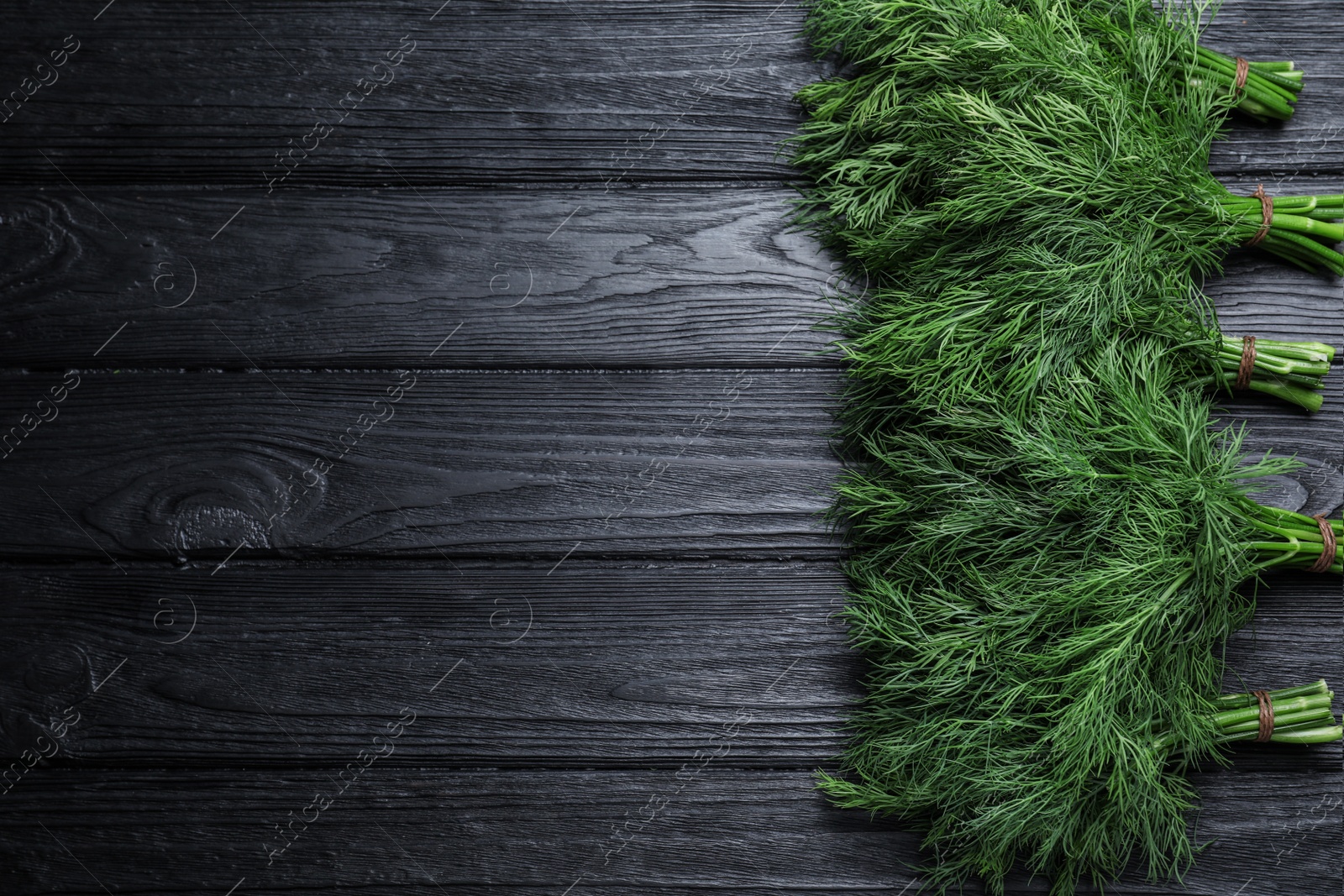 Photo of Bunches of fresh dill on black wooden table, flat lay Space for text