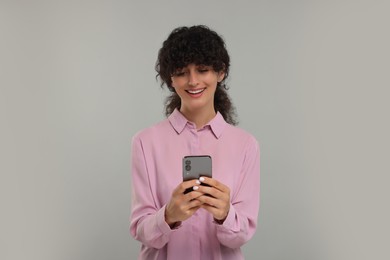 Photo of Happy young woman using smartphone on light grey background