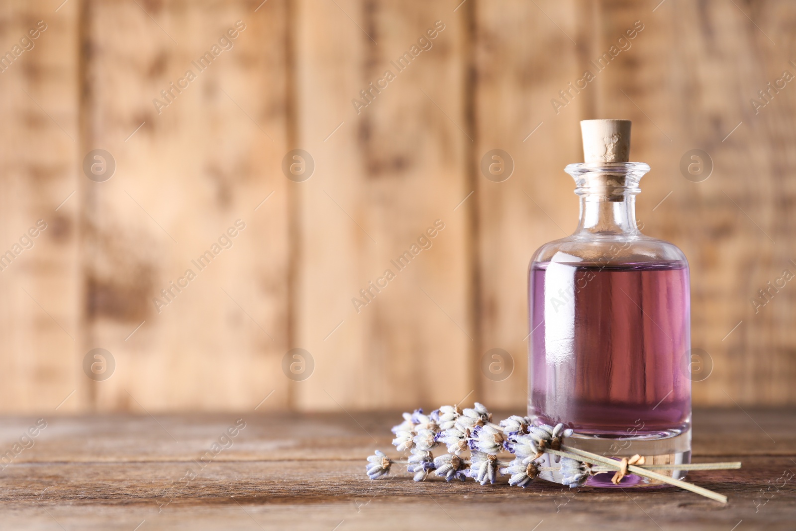 Photo of Bottle of natural essential oil and lavender flowers on wooden background. Space for text