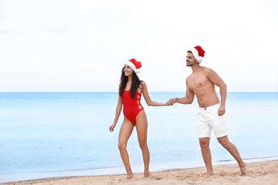 Photo of Happy young couple with Santa hats on beach near sea