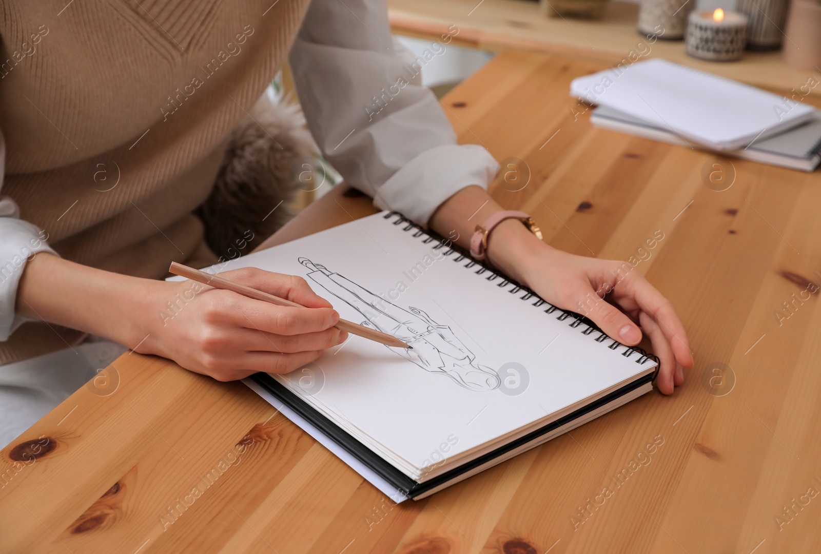 Image of Fashion designer creating new look. Woman drawing sketch in book with pencil at wooden table, closeup