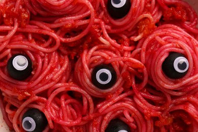 Red pasta with decorative eyes and olives as background, top view. Halloween food