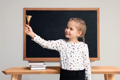 Photo of Pupil with school bell near desk and chalkboard in classroom