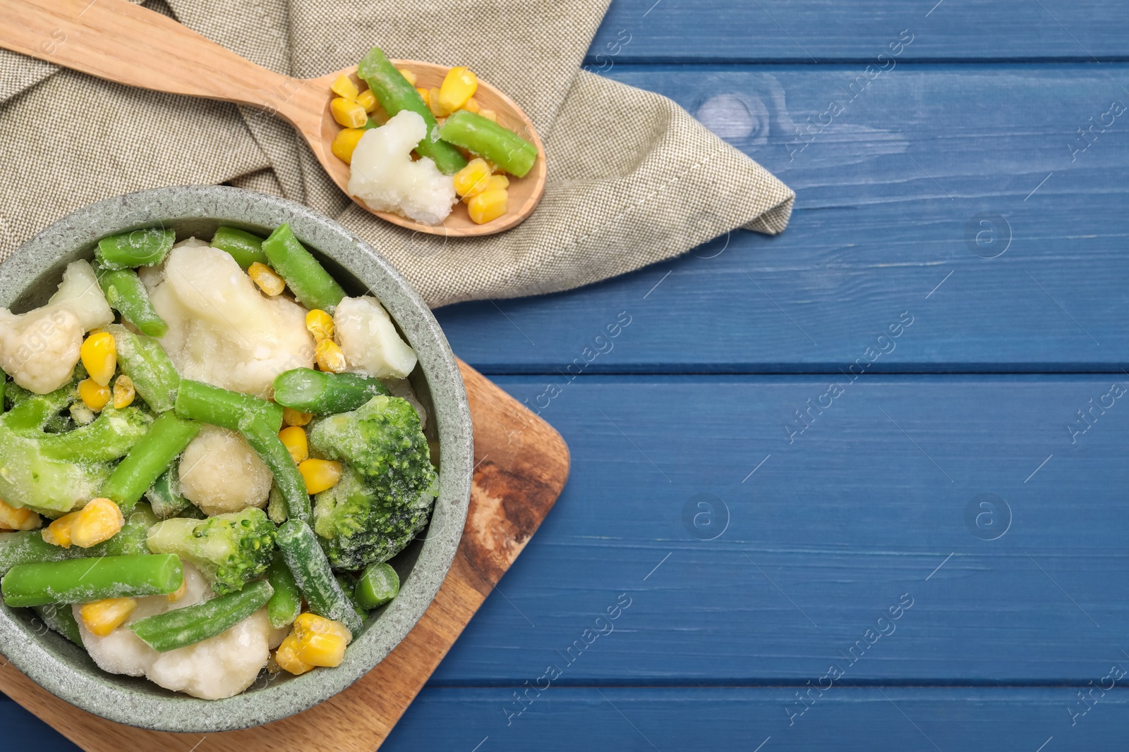 Photo of Mix of different frozen vegetables in bowl on blue wooden table, top view. Space for text