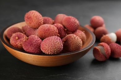 Photo of Fresh ripe lychee fruits in wooden bowl on black table
