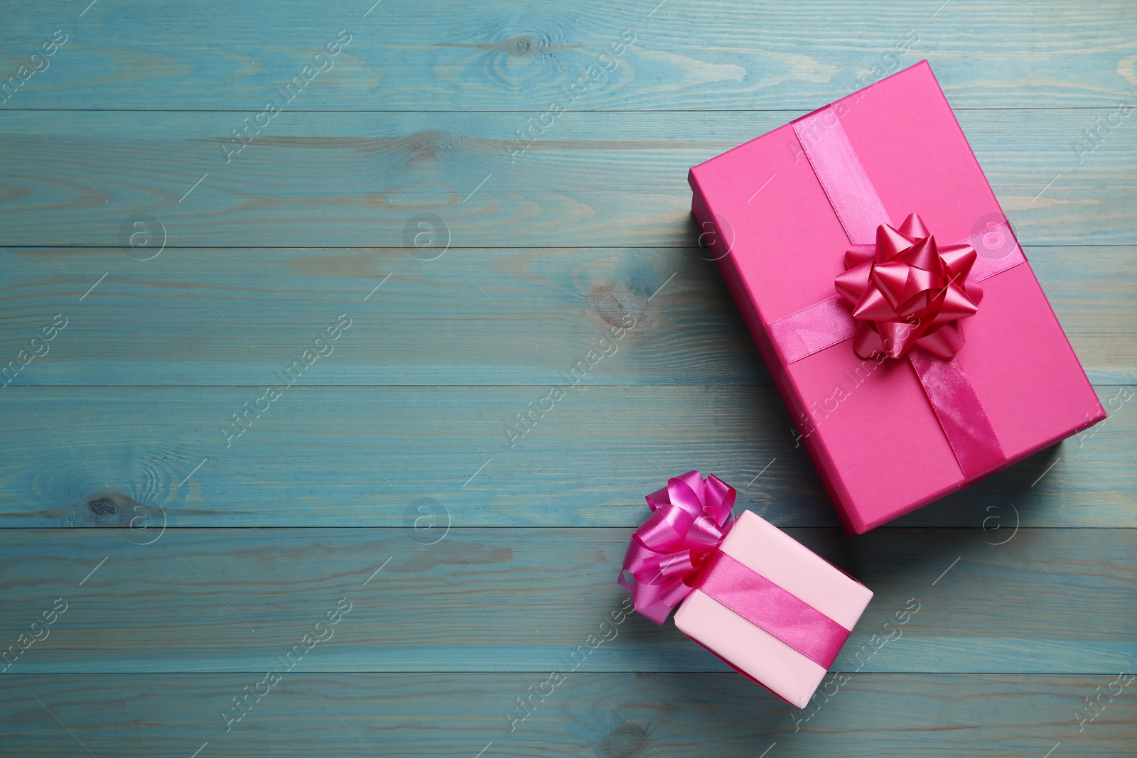 Photo of Pink gift boxes on light blue wooden table, flat lay. Space for text