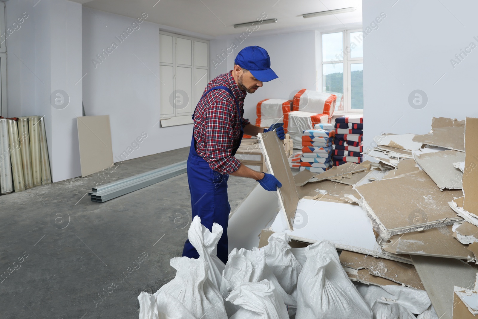 Photo of Construction worker carrying used drywall in room prepared for renovation