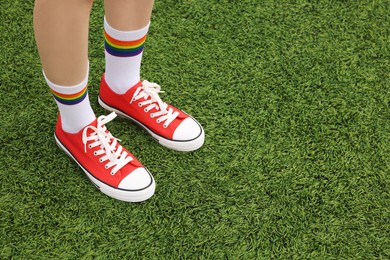 Photo of Woman wearing red classic old school sneakers on green grass outdoors, closeup. Space for text