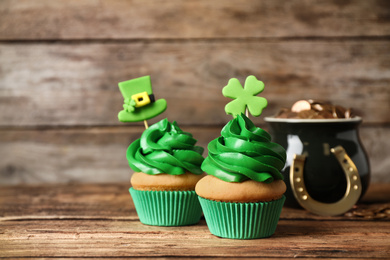 Decorated cupcakes and pot with gold coins on wooden table. St. Patrick's Day celebration