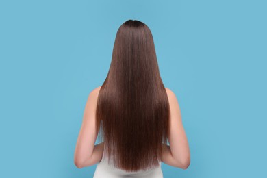 Woman with smooth healthy hair after treatment on light blue background, back view
