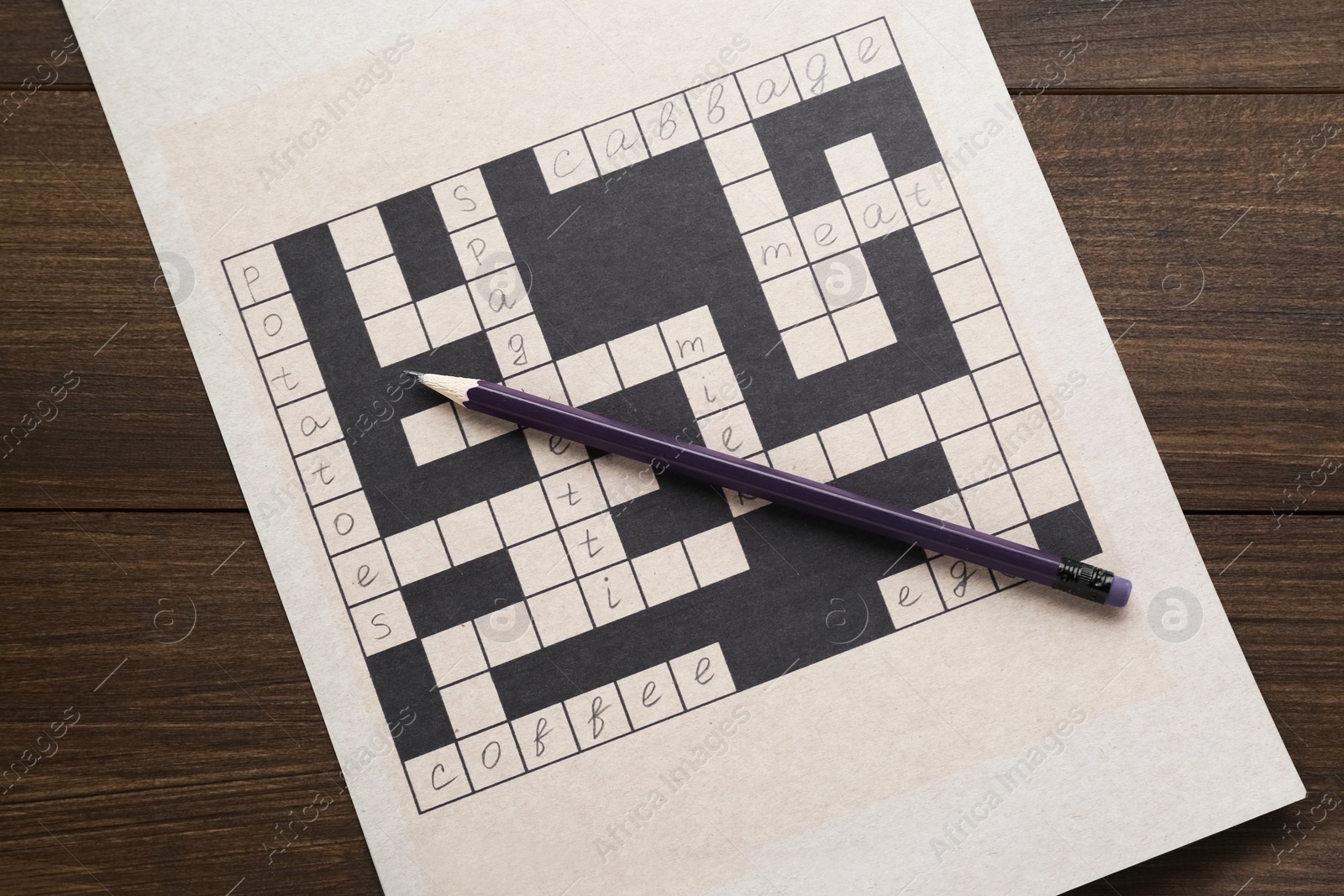 Photo of Crossword with answers and pen on wooden table, top view