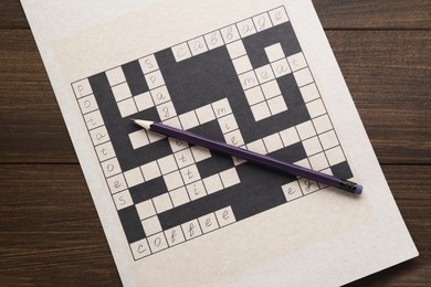 Photo of Crossword with answers and pen on wooden table, top view
