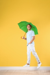 Man with green umbrella near color wall