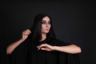 Photo of Mysterious witch in mantle with hood on black background