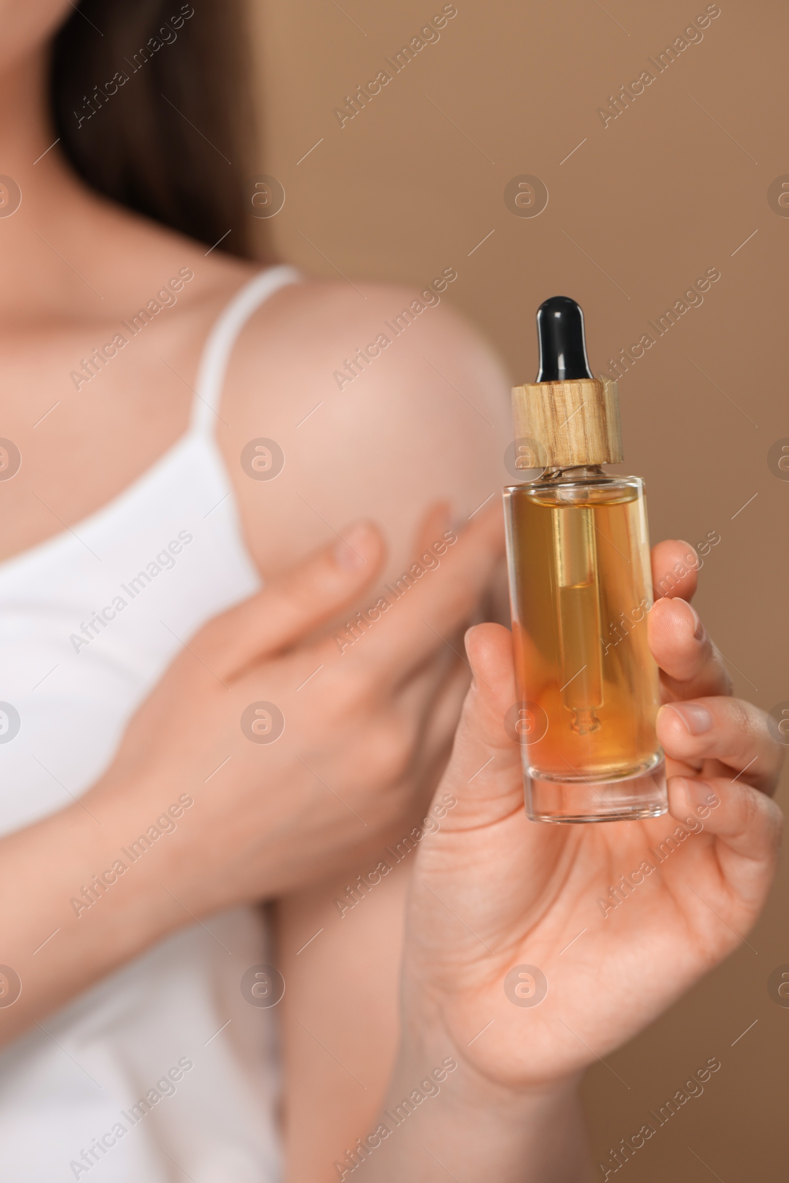 Photo of Woman holding bottle of essential oil on brown background, closeup