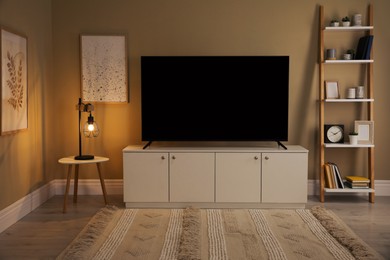 Photo of Modern TV on cabinet, white table and shelving unit near beige wall in room. Interior design