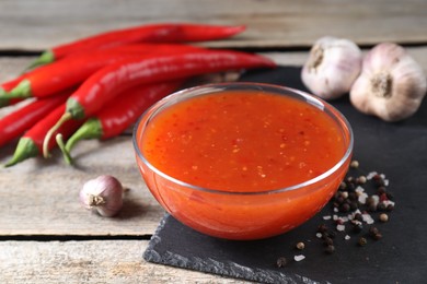 Photo of Spicy chili sauce in bowl and ingredients on wooden table, closeup