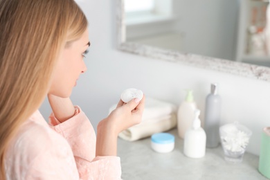 Young woman holding cotton pad with fallen eyelashes indoors