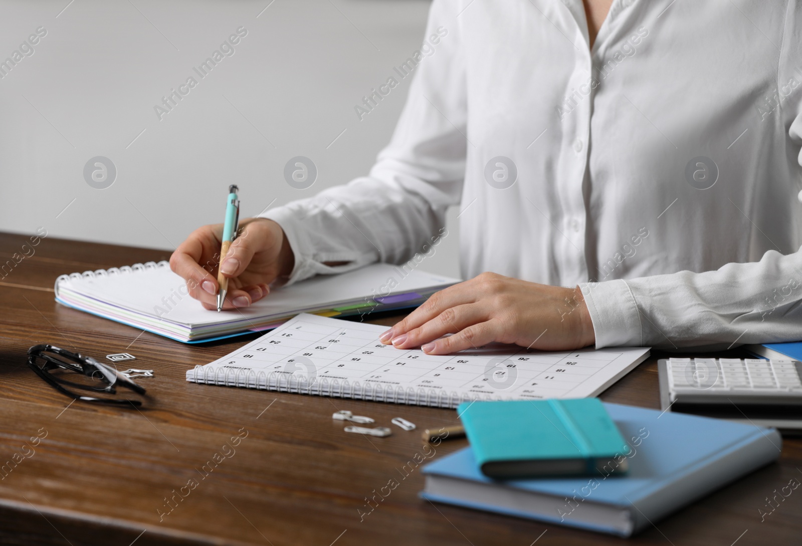 Photo of Woman making schedule using calendar at wooden table, closeup